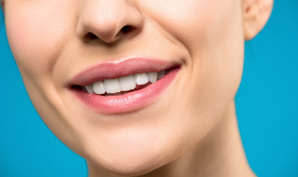 A close-up image of a woman's smile with pink lipstick and white teeth against a blue background.