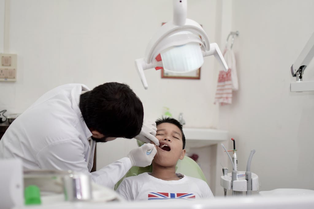 A young boy is receiving a dental checkup from a dentist wearing gloves in a clinic.