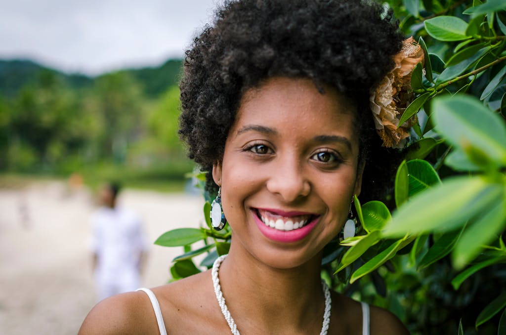 Close-up of a joyful woman smiling beside lush greenery outdoors.