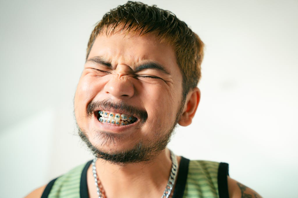 Close-up of a smiling man with braces, beard, and mustache expressing joy indoors.
