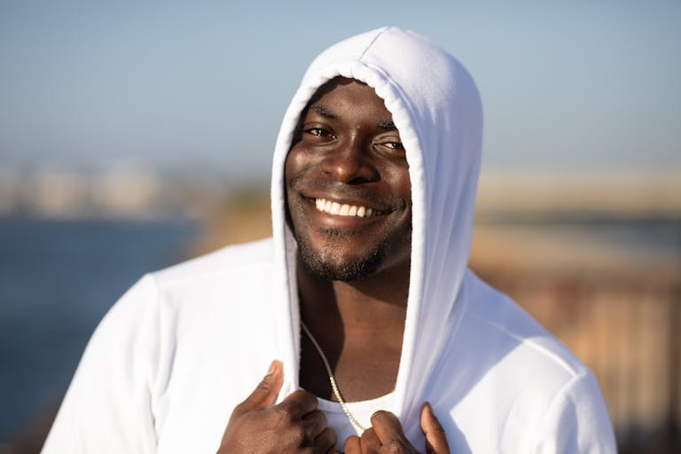 Smiling man in white hoodie enjoying a sunny day outdoors.
