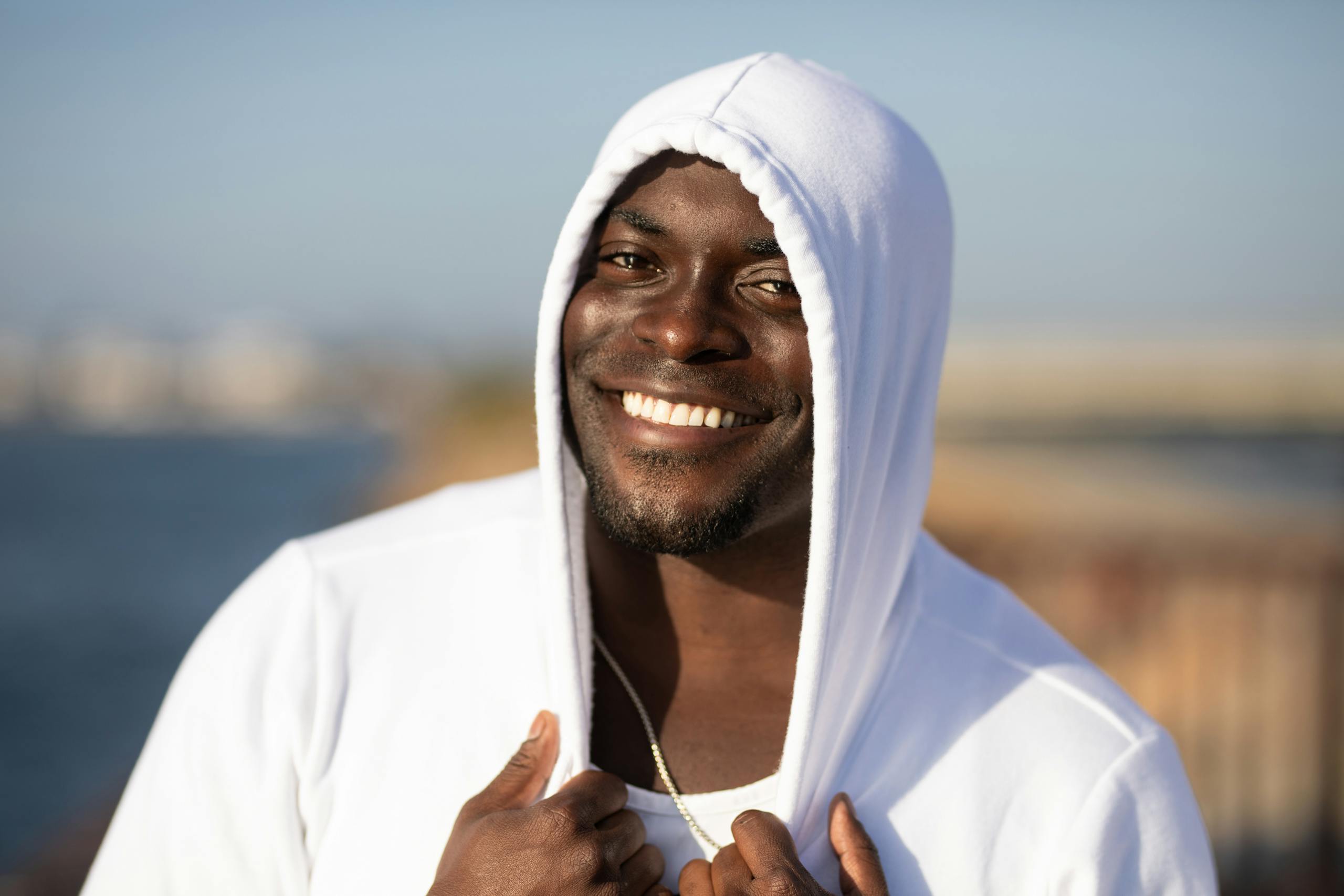 Smiling man in white hoodie enjoying a sunny day outdoors.