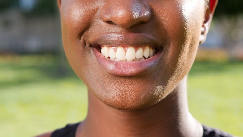 A close-up of a person smiling, showcasing their teeth and lips, captured outdoors.