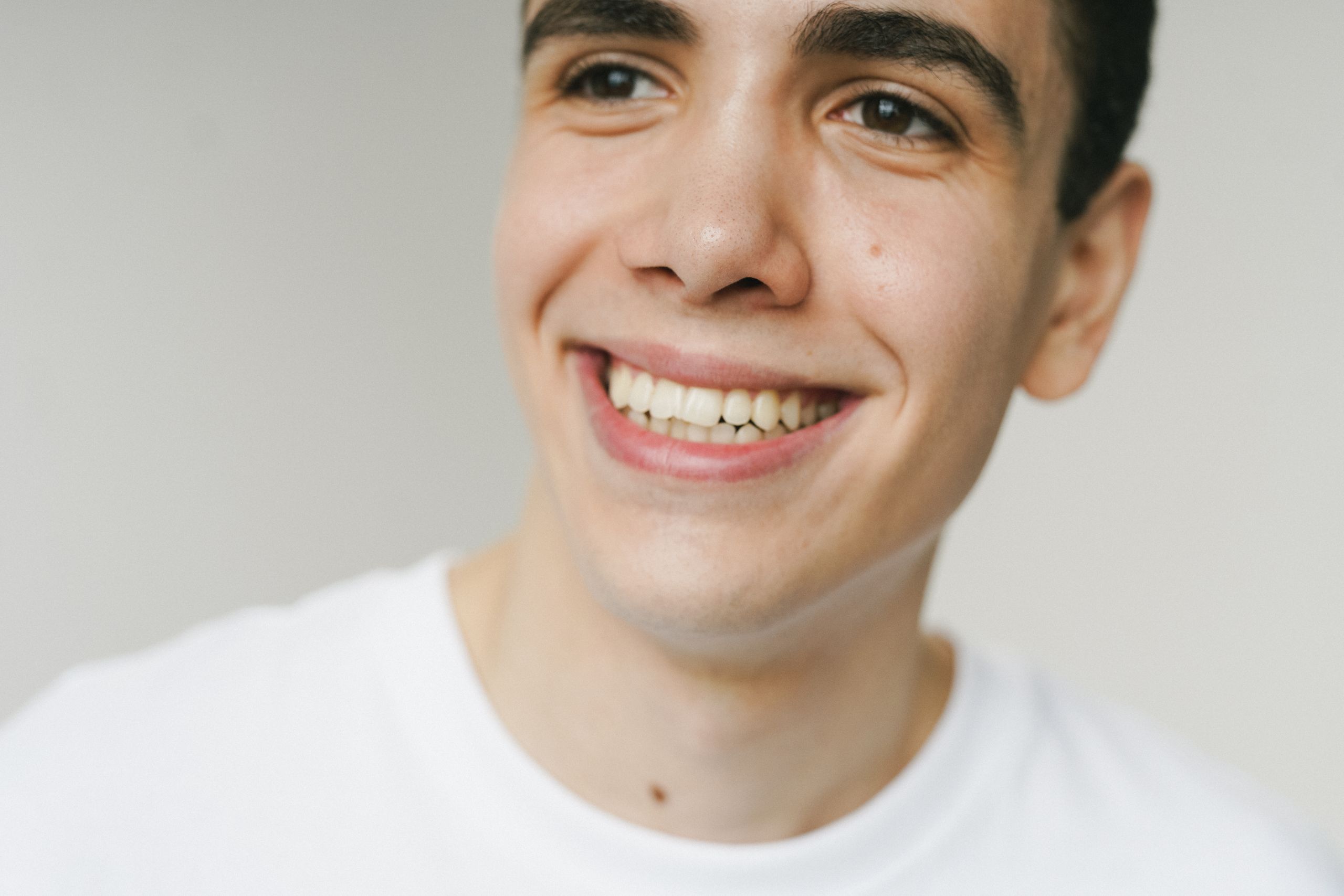 Close-up portrait of a young man smiling warmly against a light background.